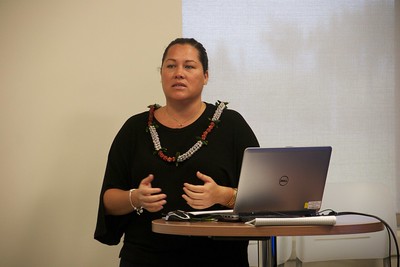 Dr. Kalikolani Correa stands at a raised table with a laptop, giving a presentation in the ‘Onipa‘a Speaker Series