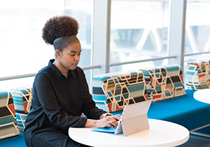 Black woman sitting on colorful couch and working on a laptop on a small table in front of her