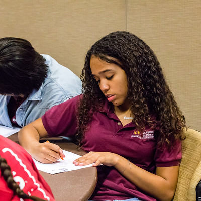 Black college student sits between two peers, all are writing on paper.